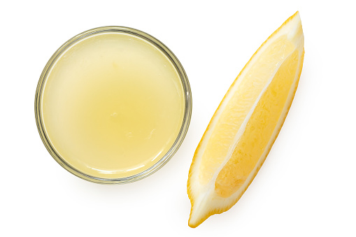 Freshly squeezed lemon juice in a glass bowl next to lemon segment isolated on white. Top view.