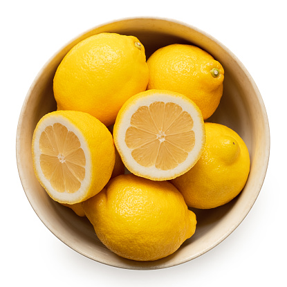 Whole and halved fresh lemons in light rustic bowl isolated on white. Top view.