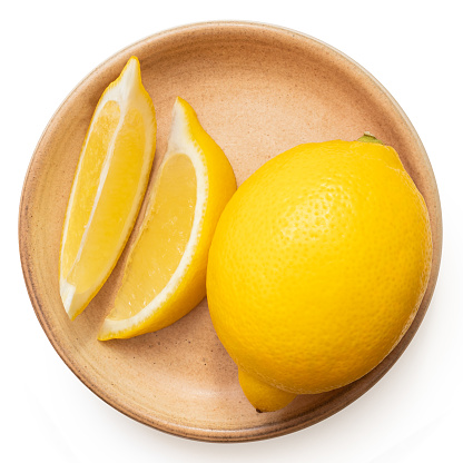 Whole fresh lemon and two segments on rustic ceramic plate isolated on white. Top view.