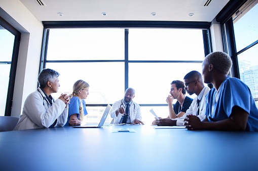 Chief physician talking with a diverse team of medical professionals during a meeting around a conference table in a hospital