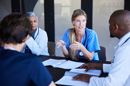 Young female doctor talking with a diverse team of medical professionals during a meeting around a conference table in a hospital