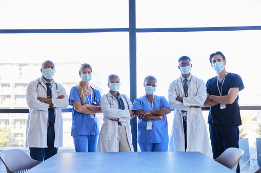 Portrait of a diverse group of doctors and surgeons wearing protective face mask standing in a hospital boardroom