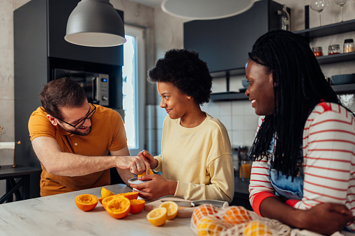 Biracial parents and daughter squeezing an orange with an orange juicer at home