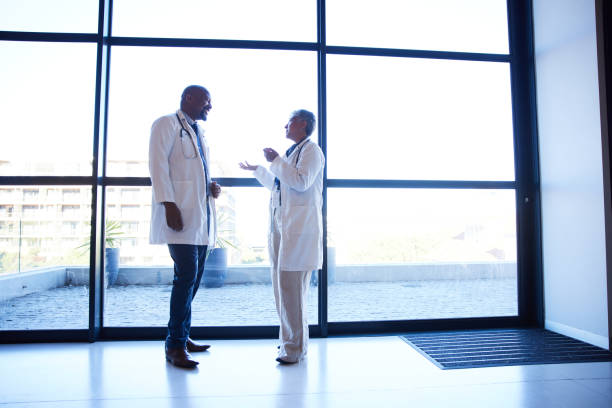 istock Smiling mature doctors talking by windows in a hospital 1396684435