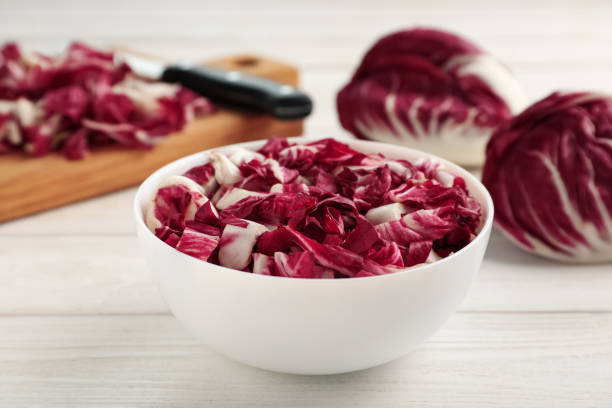 couper le radicchio dans un bol sur table en bois blanc - radicchio photos et images de collection