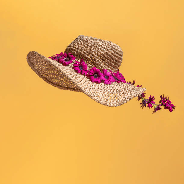 Minimal summer concept with flowers on a straw hat isolated on orange background. Square layout with copy space.
