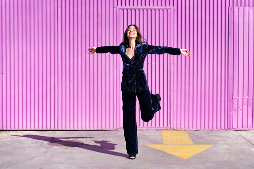 Woman wearing blue suit dancing near pink shutter. Fashion concept.