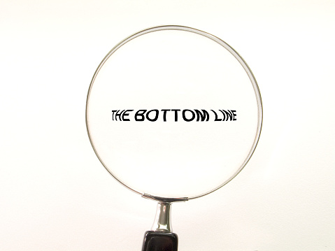 'The Bottom Line' seen under a magnifying glass. Symbolic of accounting, management, or consulting