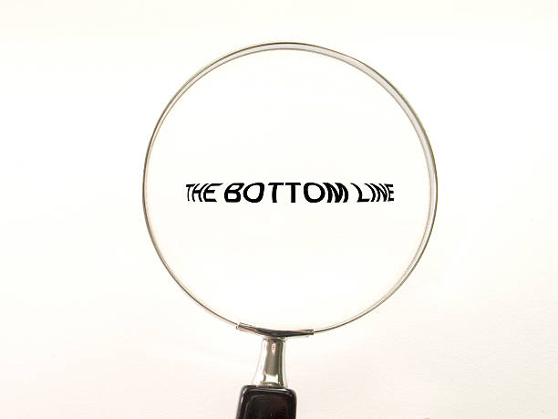 A magnifying glass over the words 'the bottom line' 'The Bottom Line' seen under a magnifying glass. Symbolic of accounting, management, or consulting at the bottom of photos stock pictures, royalty-free photos & images