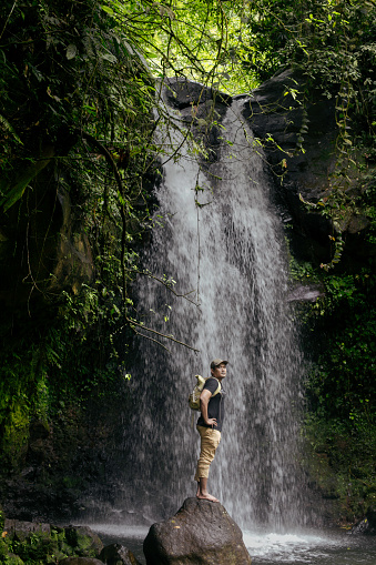 asian man walking  across a rocky surface to get to a waterfall in the forest