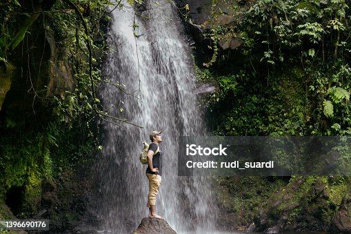 istock asian man walking  across a rocky surface to get to a waterfall in the forest 1396690176