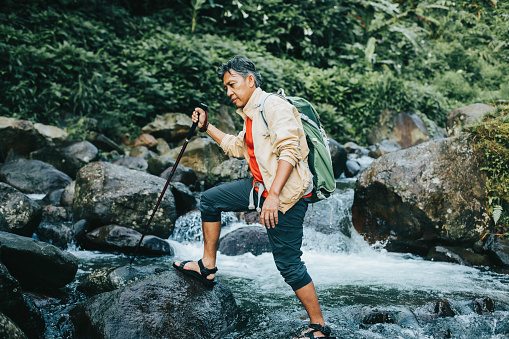 contented senior male hiker with trekking pole crossing the river