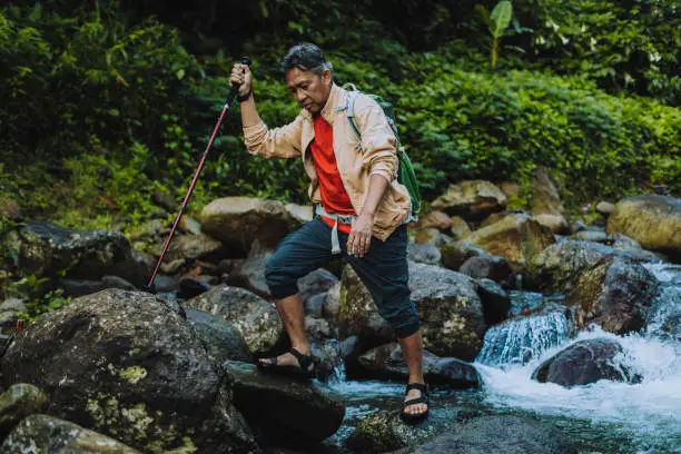 Photo of contented senior male hiker with trekking pole crossing the river