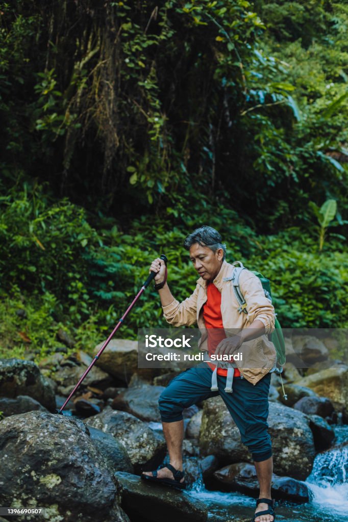 contented senior male hiker with trekking pole crossing the river Walking Stock Photo