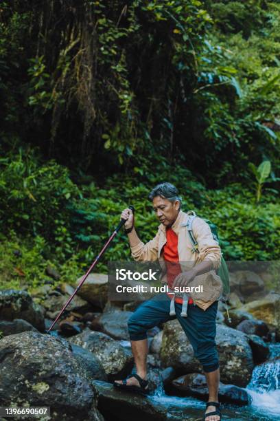 Contented Senior Male Hiker With Trekking Pole Crossing The River Stock Photo - Download Image Now