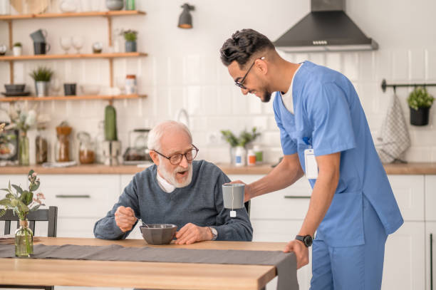 istock Cheerful caregiver serving tea to an aged man 1396691267