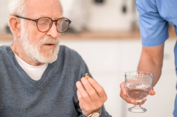 istock Pensioner taking a pill with water supervised by his caregiver 1396691278