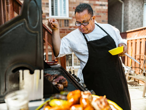 Mature Latin Chef grilling meat on BBQ in the backyard stock photo