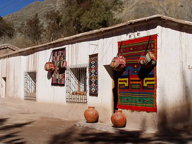 OLYMPUS DIGITAL CAMERA Beautiful colorful woven articles and clay pots decorate the front of this village store. Found in Purmamarca, Jujuy province of Argentina.