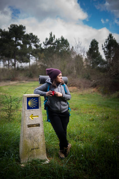 a pilgrim woman rests leaning on a sign of the Camino de Santiago a pilgrim woman rests leaning on a sign of the Camino de Santiago pilgrimage stock pictures, royalty-free photos & images