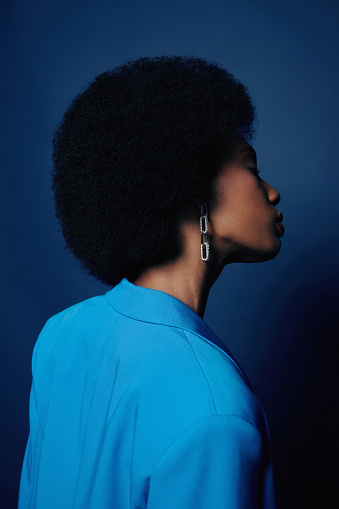 Minimal fashion shot of young black woman with puffy natural hair posing against blue background