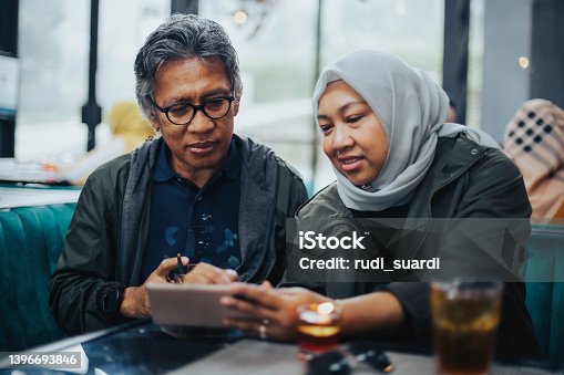 istock Smiling woman leaning on man's shoulder using digital tablet at cafe 1396693846