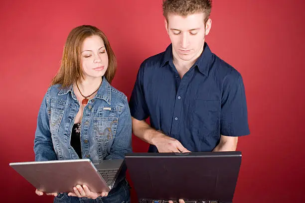 Young adult female peeking at her male counterpart's laptop screen.