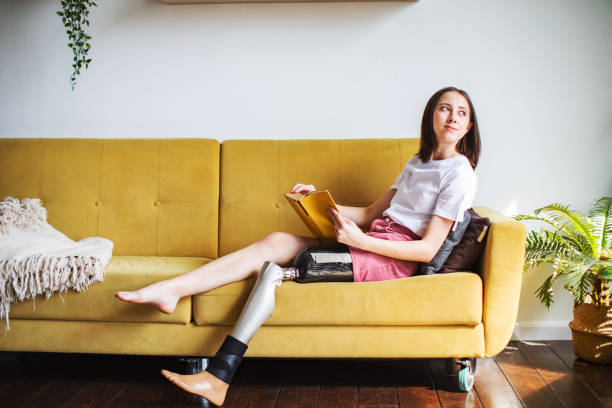 istock Young woman amputee with prosthesis reading book at home 1396694937