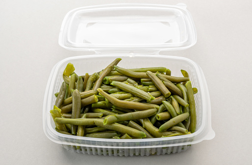 Boiled green beans in transparent food-grade plastic box for refrigeration or storing, on light gray background