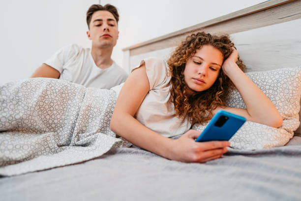 novio espiando a su novia mientras ella usa un teléfono inteligente - entrometido fotografías e imágenes de stock