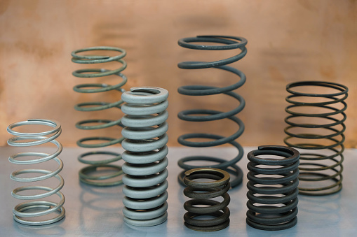 Set of springs of different size and different material on a steel surface.