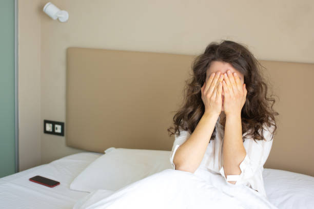 istock Stressed young woman squeezing head with hands, suffering from headache, sitting in bed at home in white pajamas after bad sleep in morning. Feeling sick.Tension or migraine health problem.Copy space 1396698066