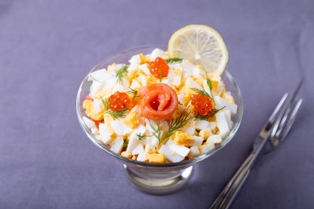 Puff salad with salted trout (salmon), red caviar, egg and vegetables. A traditional dish, one serving in a glass glass on a gray background. To