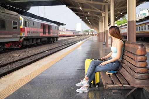 woman traveler waiting fot the train, sitting and using smartphone at train station