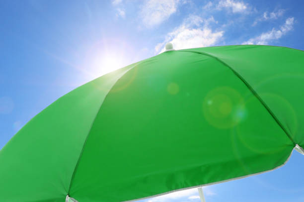 Open big green beach umbrella and beautiful blue sky with white clouds on background