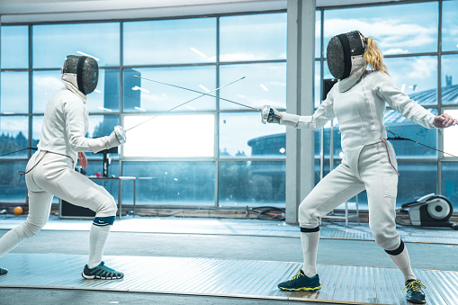 Side view of two female fencers having training in full equipment