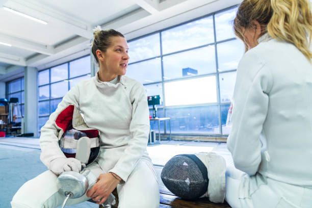 Two female fencers chat while refreshing themselves with water after a hard workout
