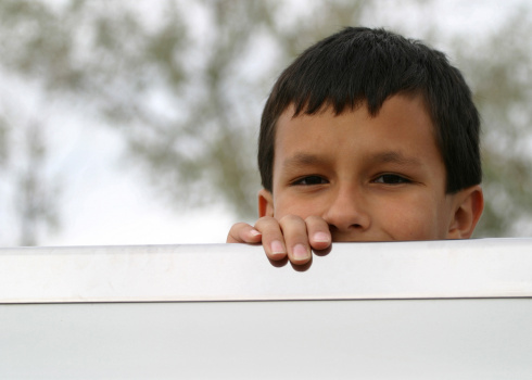 A young Latin American boy with furtive look peeks over the edge of the back of a truck bed.