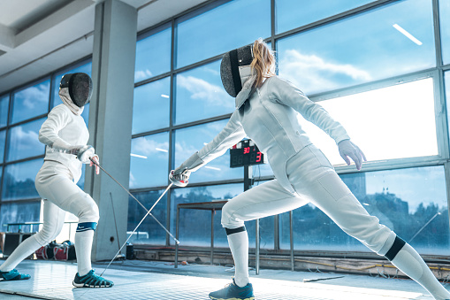 Two women wearing fencing suit practicing on professional level
