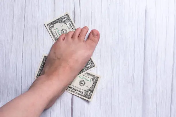 Photo of a woman's foot is stepping on dollars. Currency wrappers