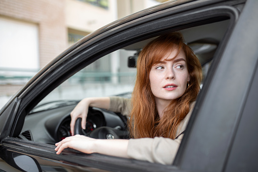 Joyful redhead woman inside of car looking back from driver seat while driving during the day.