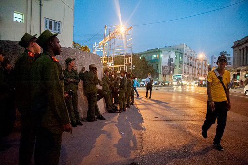 Cuban military guards on a street in Havana, Cuba near the University of Havana with a large photograph of Cuba leader Fidel Castro on a building behind them.