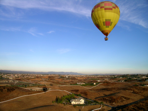 A Hot Air Ballon floats effortlessly in an azure sky above a wide open vista of California real estate. Temecula, CA.
