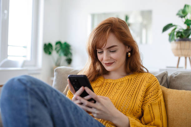 istock Smiling pretty young woman, relaxes on the sofa in her living room while using her mobile smart phone for social media and surfing the internet 1396706885