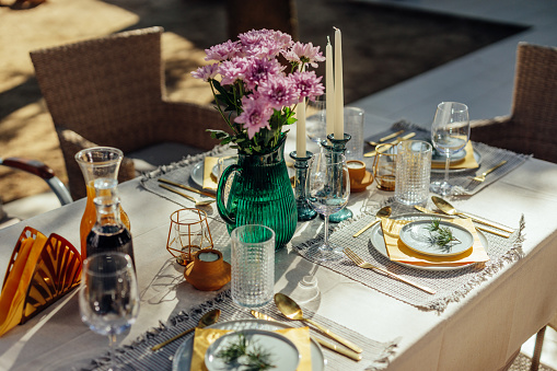 An outdoor table set for a dinner party is ready for guests to arrive. The table has custom flower bouquets going down the center of the table.
