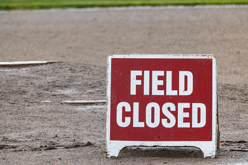 Red and white sign reading Field Closed on muddy baseball field.