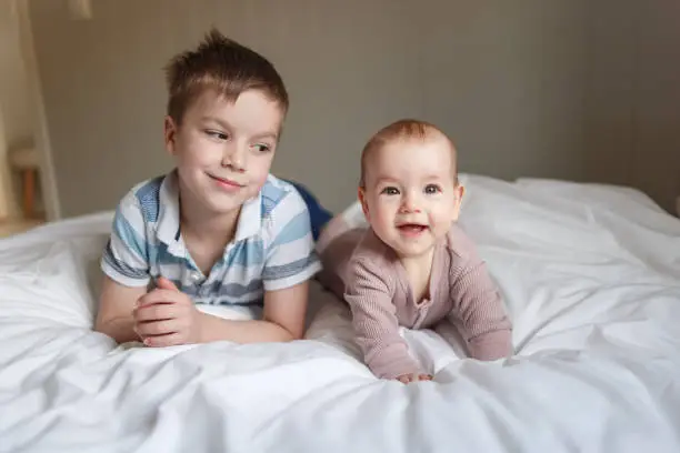 Portrait of a brother and baby sister lying on the bed at home