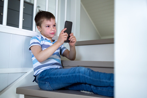 Little boy sitting on the staircase at home and looking at mobile phone