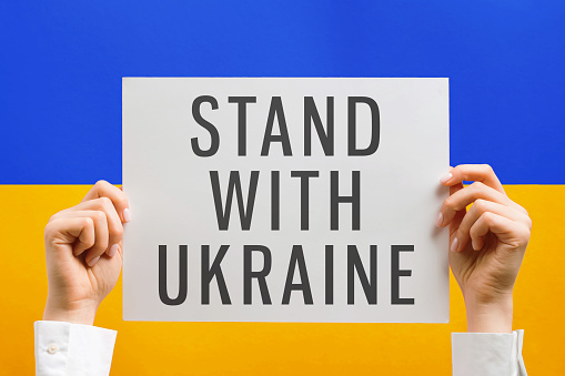 Hands holding poster with text Stand With Ukraine.