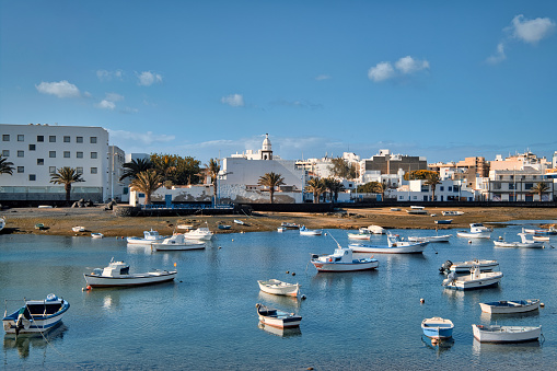 Fishing boats docked in Atlantic Ocean bay and view to the Arrecife town. Charco de san Gines. Lanzarote Island. Canaries, Spain. Travel destinations, scenic landmarks concept